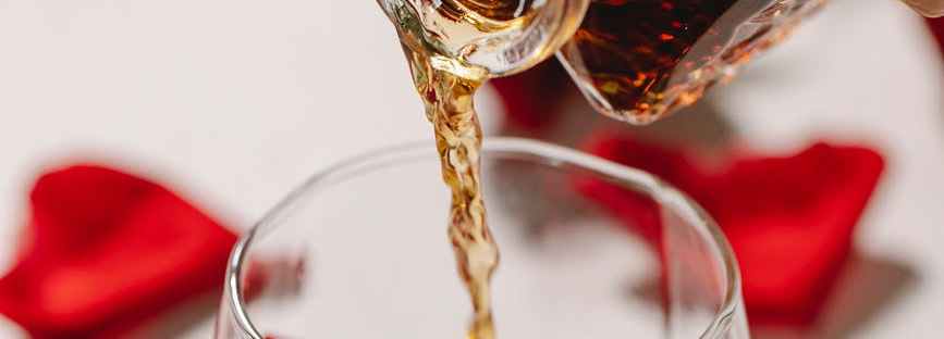 crop person pouring alcohol into glass with petals