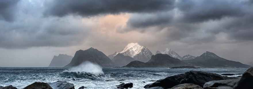 scenic view of snow capped mountains from across the rocky seashore